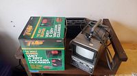 Photo showing the boxed 12V wet/dry vacuum and the portable tube TV with cables on a wooden shelf.