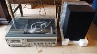 Sanyo stereo system shown alongside one stereo speaker on a concrete floor, stereo system measures approximately 21x13x8 inches, speaker is rectangular about 9x5x13 inches.