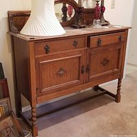 Front view of vintage oak server with ornate metal pulls on two drawers and two doors. Server stands on turned legs and has decorative trim.