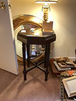 Side view of vintage wooden octagonal side table with scratches, set beside a large decorative mirror and other household items.