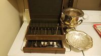 Silver plated flatware in wooden case with silver plated urn and decorative bowl visible.