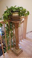 Full side view of the wooden plant stand with ceramic pot and trailing green plant on top, positioned near a wooden stair railing.