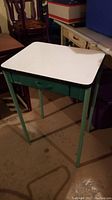 Full view of small metal table with white top and green frame, including legs and drawer front.