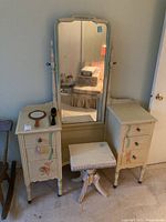 Front view of wood vanity showing mirror, two cabinet sections with drawers, and stool in front