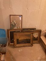 Five framed paintings grouped against wall, one floral signed Coleman, four landscapes in gold and wood frames.