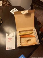 Contents of box showing brass vintage wax seal stamp and two wax sticks in yellow and orange.