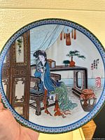 Hand held view of a porcelain plate depicting a seated woman reading by a lacquer desk