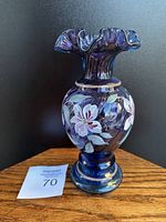 Front angle of plum opalescent glass vase showing handpainted white and lavender flowers with gold rim and signature 'Carol Griffith'.