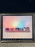Framed poster showing colorful sculptural objects on a wooden shelf with a pink and blue gradient background.