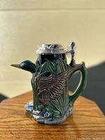 Ceramic Budweiser beer stein with mallard and cattail design, showing side and front details, lid wrapped in plastic to protect stopper.