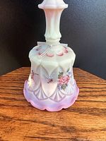 Side view of Fenton opalescent glass bell with hand painted floral design and scalloped base on wooden surface.