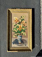 Full view of the framed flower still life painting placed on pavement, showing entire artwork and frame.