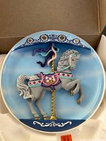 Photo of a Bradford Exchange music plate with a gray carousel horse mounted on a gold pole inside a round blue and white decorative plate.