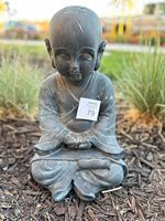 Front view of the dark grey statue depicting a young Tibetan monk in meditation with a peaceful facial expression and folded hands.