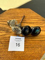 Four vintage door knobs displayed on wooden table, two clear glass and two black porcelain knobs with metal spindles/fittings.