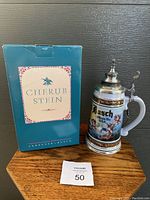 Front view of Budweiser Cherub Stein with original blue box showing label 'Cherub Stein' and part of the stein's artwork with the lid closed.