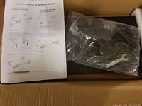 Instruction manual with product and schematic diagrams, plastic bag with mounting wrench and screws, and main bracket.