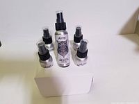 Six silver-tone bottles of Alpine brand hand sanitizer, one larger in the center with detailed owl logo, five smaller surrounding it, all with black spray tops.