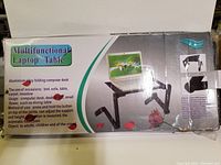 Photo of box packaging showing multifunctional laptop table with features and usage instructions.