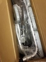 Image showing parts of the Drive Medical Transfer Tub Bench packed in a cardboard box and wrapped in plastic, including metal legs and handles.