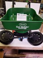 Front view of Scotts Turf Builder EdgeGuard Mini Broadcast Spreader showing green hopper and wheels with instruction manual inside hopper.