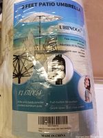 Photo of product packaging showing UHINOOS 9FT Patio Umbrella features including fade resistance, adjustable tilt, crank open and close system, powder-coated aluminum pole, and 8 ribs.