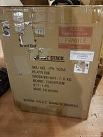 Photo of the product shipping box labeled as wooden puzzle board with 6 drawers, SKU PV 1006, gross weight 7.5 kg, dimensions 73x5x93 cm, made in China, marked fragile.