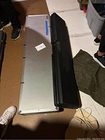 Two long cases side by side on floor: the longer Aluma-Max aluminum case and shorter black plastic Guard case
