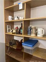 Wooden shelving unit with various items including two German beer steins, ISS Henley mug, vintage military flight cap, goggles, and small art objects.
