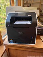 Front view of Brother color laser printer with touchscreen and output tray holding printed sheet