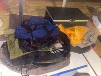 Wide view of assorted camping bags and backpacks with a green Coleman cooler in the background.