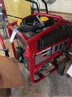Angled front view of red tubular frame generator with fuel tank, controls and wheels in garage