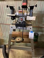 Front view showing the bench grinder with dual grinding wheels and mounted on the metal stand.