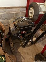 Side view of the black and red Craftsman leaf blower with visible engine and wheels on a concrete garage floor.
