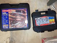 Two Craftsman mechanics tool sets in their closed black hard plastic cases with labels showing contents and piece count