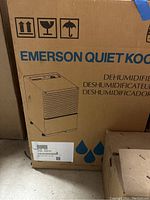 Photo of the cardboard box for Emerson Quiet Kool dehumidifier showing brand name and illustration of the unit with model number.