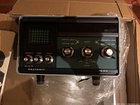 Heathkit SB-614 device showing front control panel and CRT screen inside original box with plastic wrap.