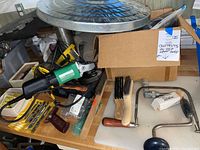 Hitachi disc grinder with drill bits and wire brushes on a wooden table, showing assortment of tools.