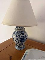 Blue and white floral porcelain lamp with cream fabric shade on wooden table, partial view of blue and white platter beside it.