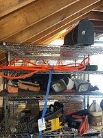 Full view of three metal wire shelves displaying lot: including orange extension cord, brushes, handheld tools, fire extinguisher, mailbox, McCulloch chainsaw and more.