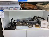 Shelf with various tools and a leather tool belt on top shelf, multiple tools and trays on lower shelves.