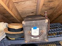 Top view of textured hard case containing the projector, next to stacks of classic hats and a leather-like covered bottle.