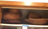 Shelf with four wicker baskets stacked inside each other, two gold-toned serving platters, and one large rustic wooden bowl