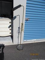 Full view of the brass adjustable floor lamp standing next to a white cabinet and blue storage door, showing the tall slender pole, round base, and adjustable arm with lampshade.