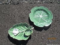Top view of green glazed cabbage leaf shaped plate and green leaf chip and dip bowl on asphalt ground showing detailed raised leaf veins and shapes.