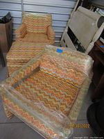 Low profile club chair and ottoman with retro patterned fabric, wrapped in plastic for protection.