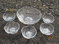 Overview of one large and five smaller crystal bowls arranged on asphalt surface. All bowls are clear with etched fruit designs.
