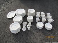 Overview of the full set displayed on pavement showing multiple stacks of octagonal white ironstone plates, cups and other pieces arranged orderly.