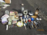 Wide view of all kitchen items laid out including knife block, pans, mugs, utensils, placemats, and other accessories.