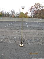 Full view of the floor lamp standing outdoors on gravel, showing its full height and base.